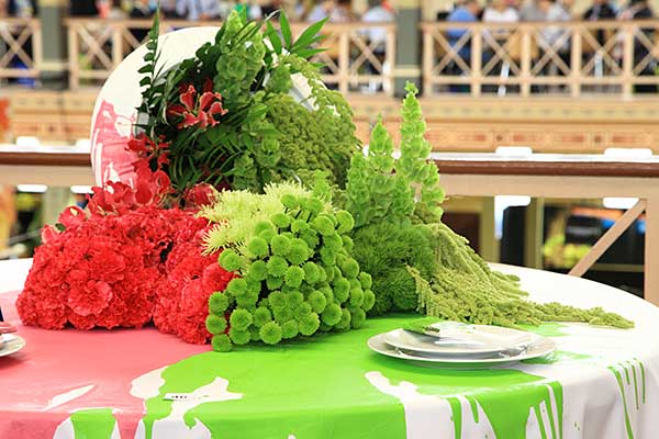 Flowers in green and pink with green and pink paint spilled on the table below them to match.