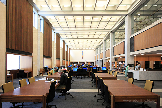 Large reading room with people reading books at tables or searching information on computers.