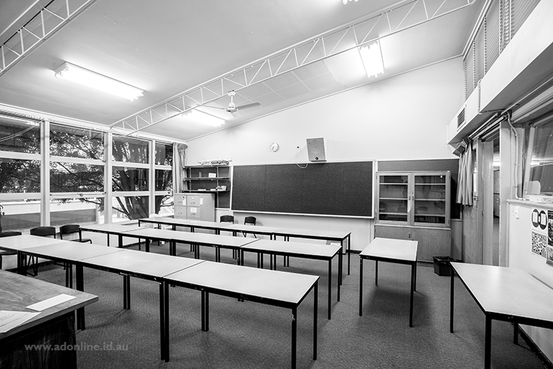 Interior of classroom showing blackboard and tables and chairs.