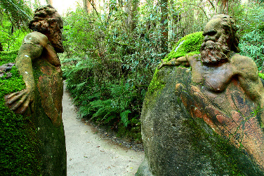 Looking down path in forest past two large boulders each with Aboriginal men carved in them
